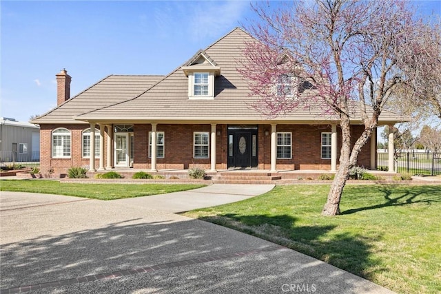 view of front of house with brick siding, covered porch, a front yard, and fence