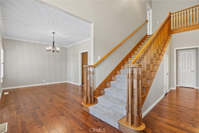 stairs featuring hardwood / wood-style floors, a notable chandelier, baseboards, and ornamental molding