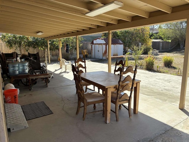 view of patio with a fenced backyard, outdoor dining space, a storage unit, and an outdoor structure