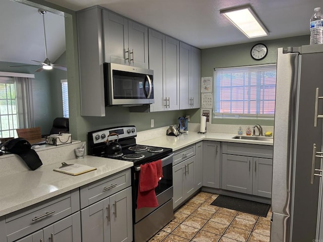 kitchen featuring gray cabinetry, a ceiling fan, a sink, stainless steel appliances, and light countertops