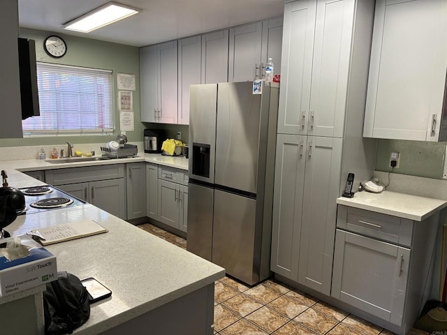 kitchen featuring gray cabinetry, light countertops, stainless steel refrigerator with ice dispenser, and a sink