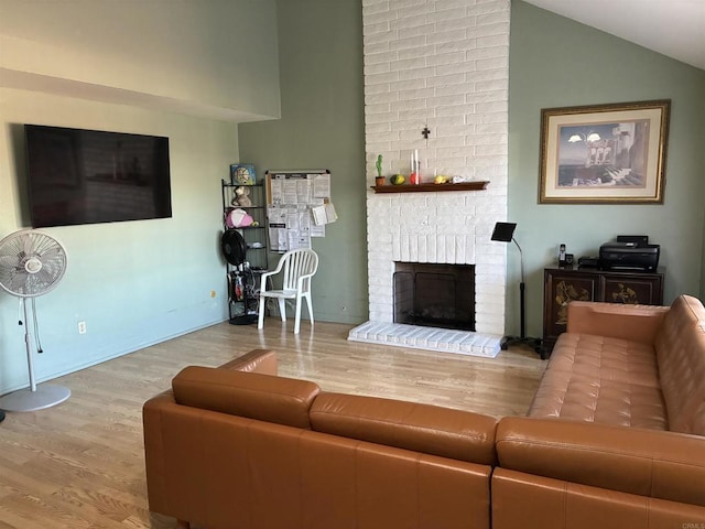 living area with high vaulted ceiling, a brick fireplace, and wood finished floors