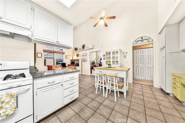 kitchen featuring under cabinet range hood, gas range gas stove, white cabinets, and a ceiling fan