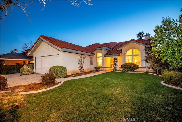 mediterranean / spanish-style house with stucco siding, a tile roof, a front yard, a garage, and a chimney