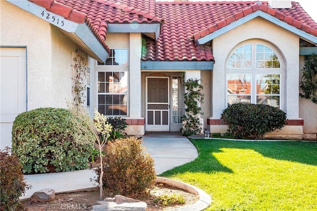 entrance to property with a tile roof, a lawn, and stucco siding