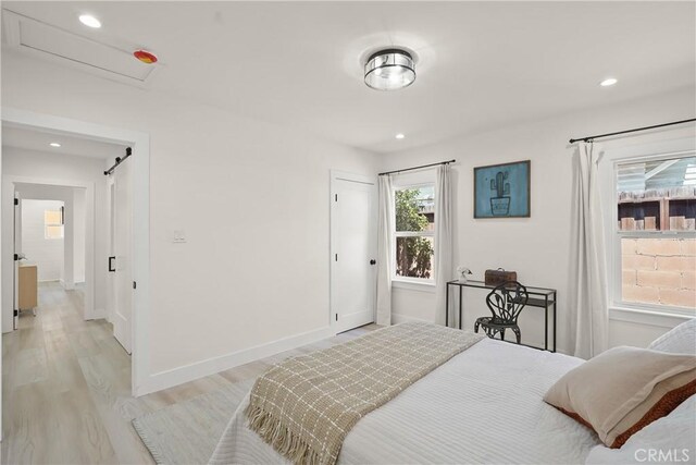 bedroom with recessed lighting, baseboards, light wood-style floors, and a barn door