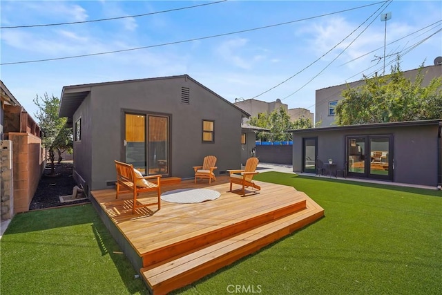 back of property with a wooden deck, a lawn, fence, and stucco siding