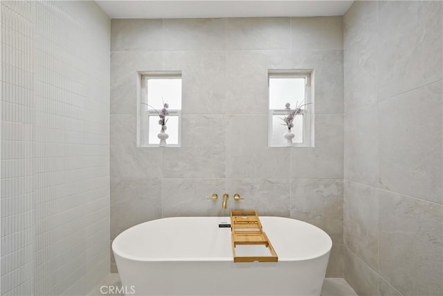 bathroom with a wealth of natural light, a freestanding tub, and tile walls