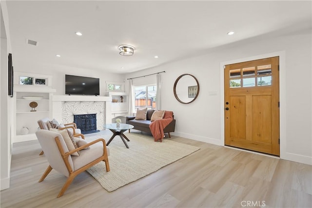 living room featuring wood finished floors, visible vents, baseboards, recessed lighting, and a stone fireplace