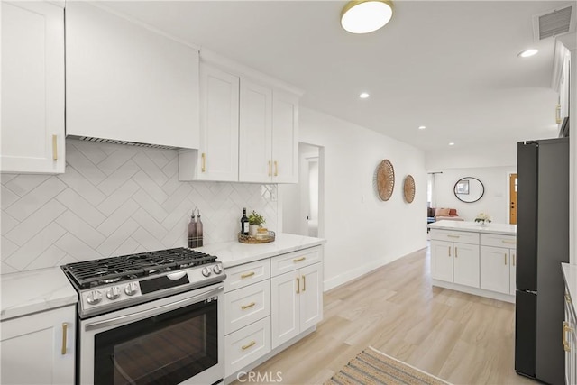 kitchen with visible vents, stainless steel range with gas stovetop, freestanding refrigerator, light wood-style floors, and white cabinetry