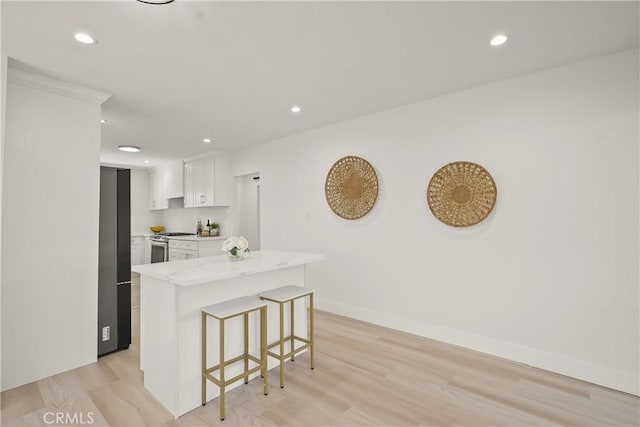 kitchen featuring stainless steel range with gas cooktop, refrigerator, light wood-style flooring, recessed lighting, and a kitchen breakfast bar