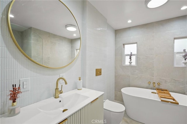 full bathroom featuring vanity, recessed lighting, a freestanding bath, tile walls, and toilet