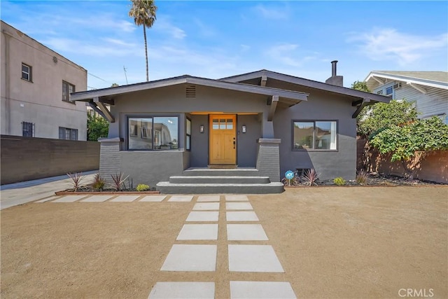 view of front of property with stucco siding, a chimney, and fence