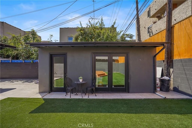 rear view of property featuring stucco siding, french doors, a yard, and fence