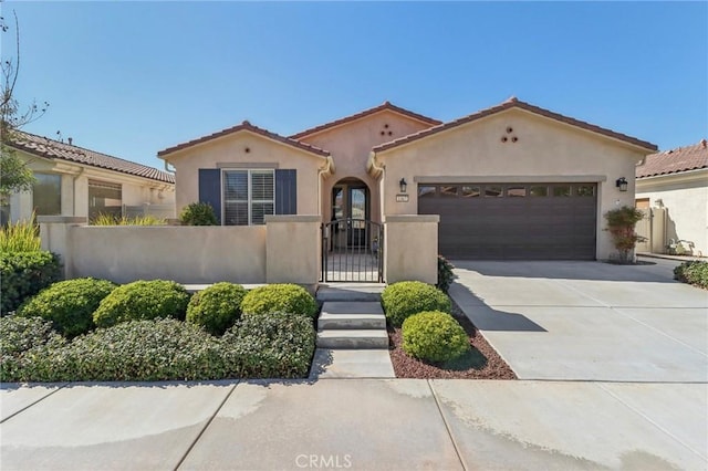 mediterranean / spanish-style home with stucco siding, an attached garage, concrete driveway, and a gate