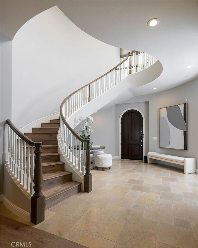 foyer entrance featuring stairway, stone tile floors, recessed lighting, a high ceiling, and arched walkways