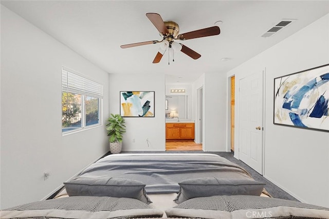 carpeted bedroom with connected bathroom, baseboards, visible vents, and ceiling fan