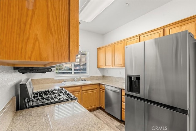 kitchen featuring light wood finished floors, stainless steel appliances, light countertops, and a sink