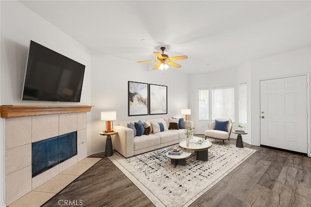 living area featuring a tiled fireplace, wood finished floors, baseboards, and a ceiling fan