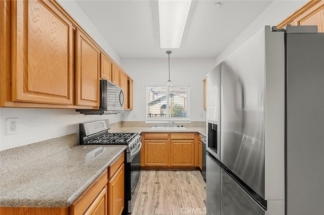 kitchen featuring light wood finished floors, a sink, gas range oven, stainless steel refrigerator with ice dispenser, and decorative light fixtures