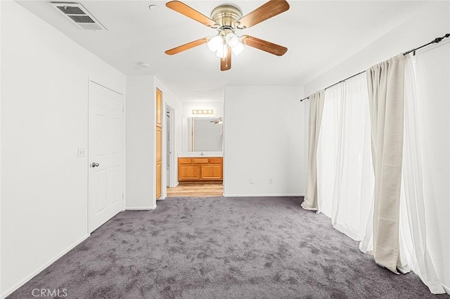 unfurnished bedroom featuring visible vents, baseboards, carpet floors, ensuite bath, and a ceiling fan