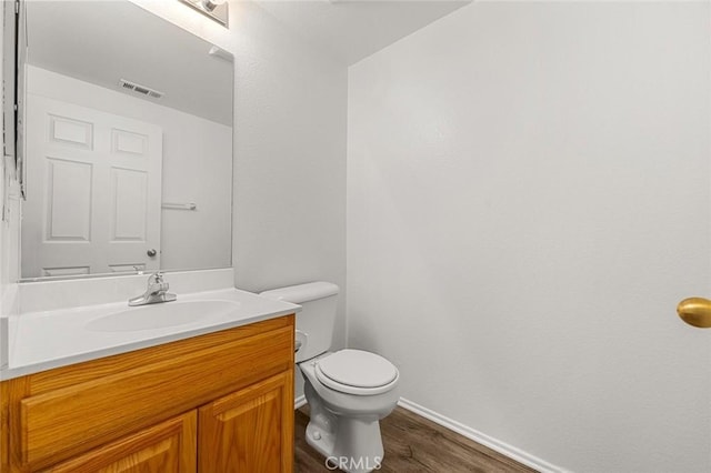 half bathroom with visible vents, toilet, wood finished floors, baseboards, and vanity