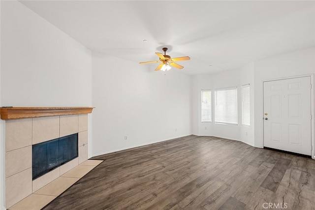 unfurnished living room with ceiling fan, baseboards, light wood finished floors, and a tile fireplace