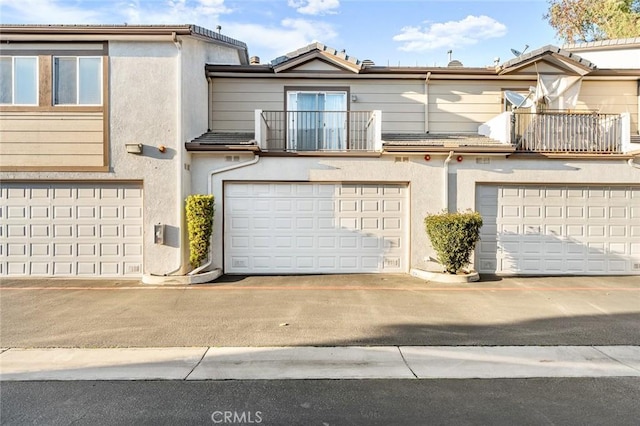 view of front of house with stucco siding, a balcony, an attached garage, and a tiled roof