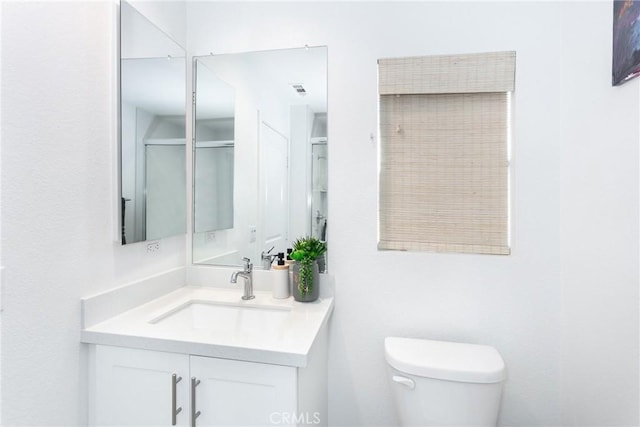 bathroom featuring toilet, vanity, and a shower with shower door