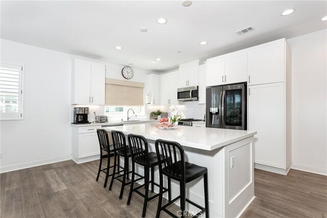 kitchen with visible vents, dark wood finished floors, a center island, appliances with stainless steel finishes, and a breakfast bar area