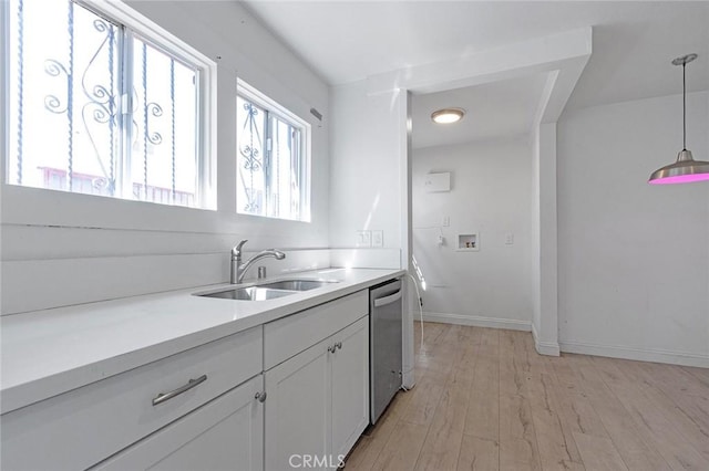 kitchen featuring light wood-style flooring, a sink, stainless steel dishwasher, white cabinets, and hanging light fixtures