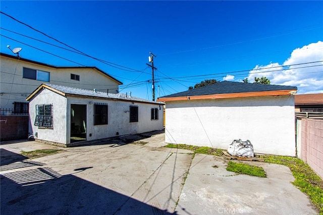 rear view of property with an outbuilding, stucco siding, a patio, and fence