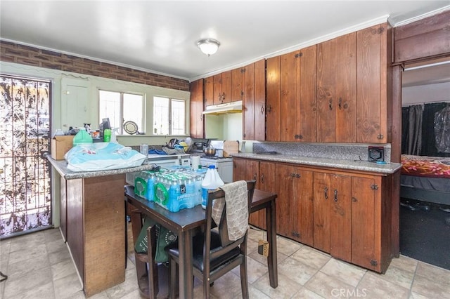 kitchen with brick wall, under cabinet range hood, white range with gas stovetop, light countertops, and brown cabinets