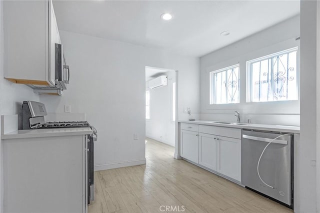 kitchen featuring a wall mounted AC, a sink, light countertops, light wood-style floors, and appliances with stainless steel finishes