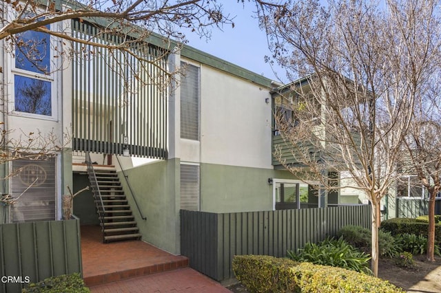 view of property exterior with stairway, stucco siding, and fence