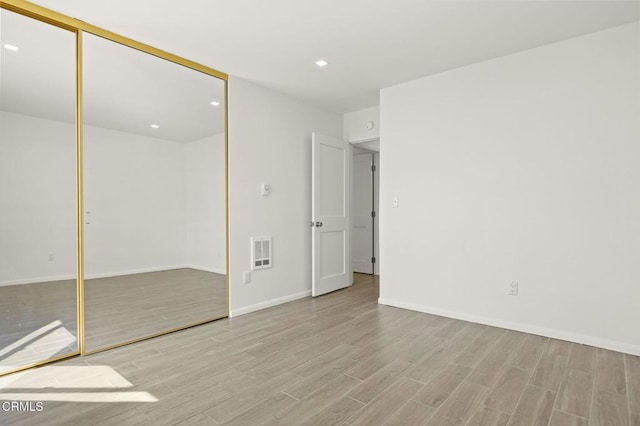 unfurnished bedroom with wood finished floors, visible vents, baseboards, recessed lighting, and a closet