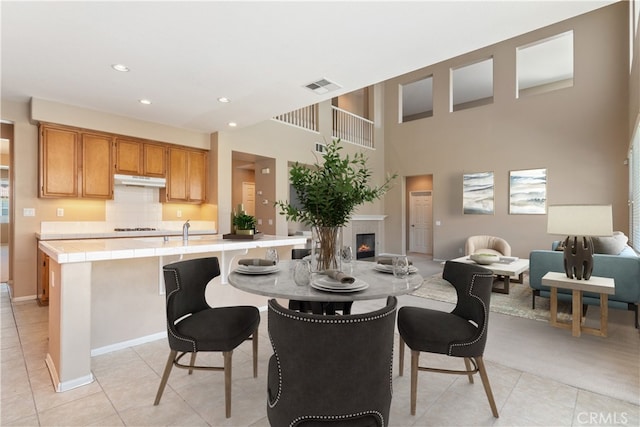 dining room featuring light tile patterned floors, visible vents, a high ceiling, recessed lighting, and a glass covered fireplace