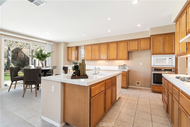 kitchen featuring visible vents, light tile patterned flooring, brown cabinetry, white appliances, and a sink