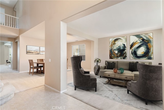 living area featuring light carpet, light tile patterned floors, baseboards, and a towering ceiling