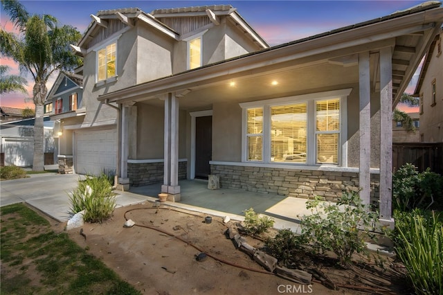 exterior space with a porch, a garage, stone siding, and stucco siding