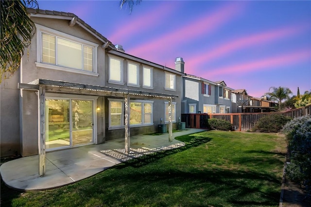 rear view of property featuring a patio, fence, central AC, stucco siding, and a lawn