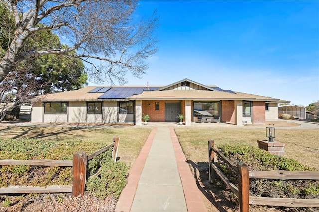 single story home featuring a front yard, fence, solar panels, brick siding, and board and batten siding