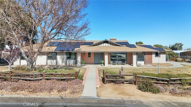 ranch-style home featuring a fenced front yard, roof mounted solar panels, brick siding, and a chimney