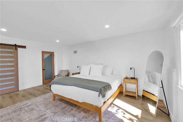 bedroom featuring a barn door, recessed lighting, wood finished floors, and visible vents