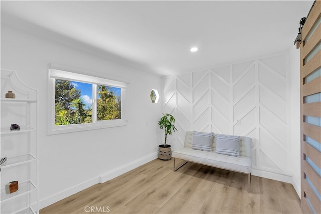 living area with a barn door, a decorative wall, baseboards, and light wood finished floors