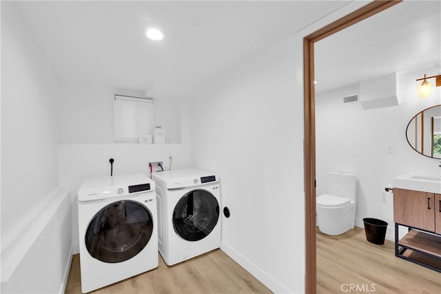 clothes washing area with visible vents, washing machine and dryer, laundry area, and light wood-style flooring