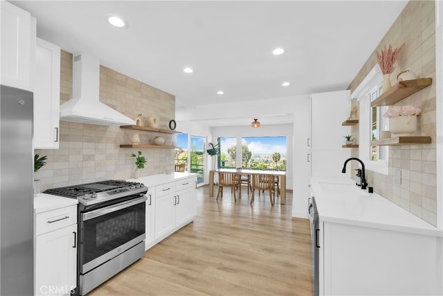 kitchen featuring open shelves, a sink, stainless steel appliances, wall chimney exhaust hood, and light wood finished floors