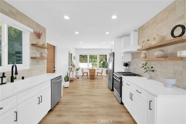 kitchen featuring light wood-style flooring, open shelves, a sink, appliances with stainless steel finishes, and wall chimney exhaust hood