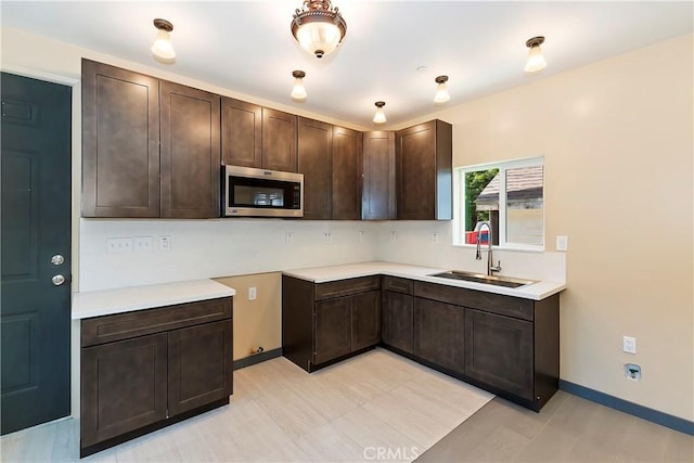 kitchen with stainless steel microwave, dark brown cabinets, light countertops, and a sink