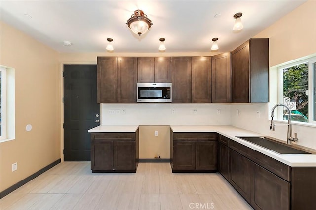 kitchen with stainless steel microwave, dark brown cabinets, light countertops, and a sink